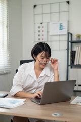 Cheerful businesswoman in white shirt using smartphone with laptop and documents on her office desk.