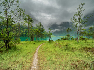 Fototapeta premium A view to the Berchtesgaden Königssee lake which have crystal clear drink water quality embedded in green nature with foggy rain cloud background
