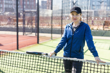 One woman with racquet and ball behind the net in paddle tennis court ready for training