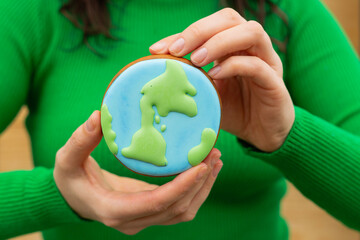 Earth Day concept. Gingerbread in the shape of a planet in the hands of a woman. - 782919341