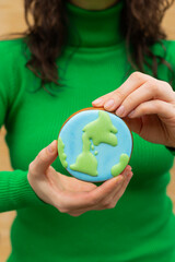Earth Day concept. Gingerbread in the shape of a planet in the hands of a woman. - 782919366