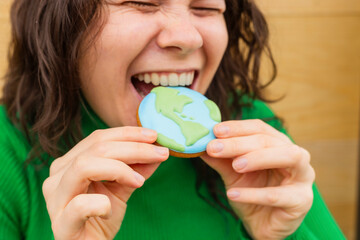 Earth Day concept. Woman bites into a cookie in the shape of the Earth.