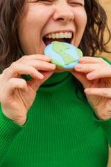 Earth Day concept. Woman bites into a cookie in the shape of the Earth.
