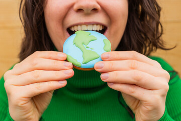 Earth Day concept. Woman bites into a cookie in the shape of the Earth. - 782919599