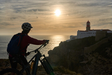 happy active senior woman cycling during moody golden hour near sunset at the the rock cliffs and...