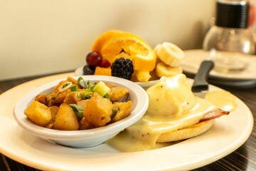 Closeup shot of Patatas Bravas and Eggs Benedict with fruits in background