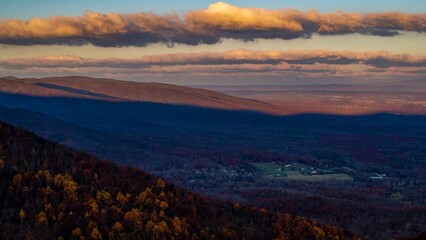 Sunset landscape of an autumn forest with buildings hidden in trees on the backdrop of mountains