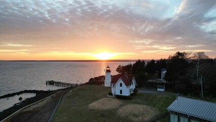 Drone shot of splendid sunset over the sea and a lighthouse next to a home on the shore