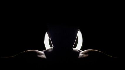 Silhouette of the shoulders of an athletic man in front of a light on a dark background - obrazy, fototapety, plakaty