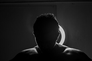 Silhouette of the shoulders of an athletic man in front of a round light, a grayscale shot