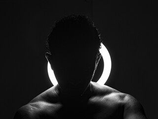 Silhouette of the shoulders of an athletic man in front of a light,  a a grayscale shot