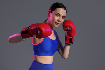 Portrait of beautiful woman wearing boxing gloves in color lights on grey background