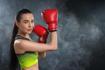Beautiful woman wearing boxing gloves training in smoke on black background. Space for text