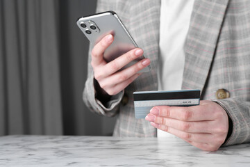 Online payment. Woman with smartphone and credit card at white marble table, closeup
