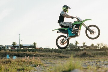 Biker man with a helmet riding a motocross bike and doing the wide-open skill in rural field