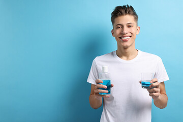 Young man with mouthwash on light blue background, space for text