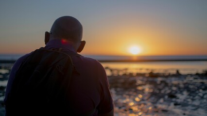 Back view of a man with a backpack admiring the view of the sunset