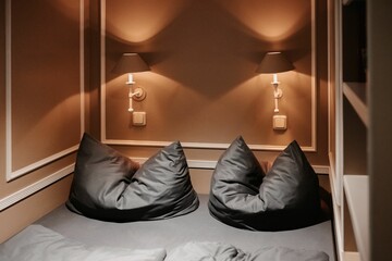 Bed with two gray pillows and lamps on the brown walls in a small room
