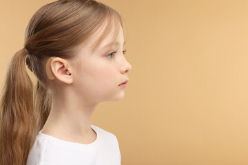 Little girl with hearing aid on pale brown background. Space for text