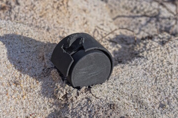 one small black plastic wheel for a luggage bag lies in the gray sand on the street