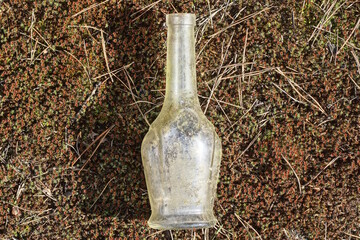 one small dirty white glass bottle lies on brown green moss on the street