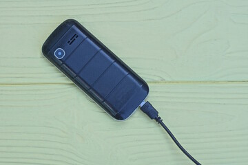 one retro mobile phone with a black plastic cover with a wire lies on a yellow wooden table