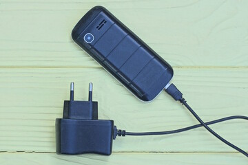 one old black mobile phone and charger lie on a yellow wooden table