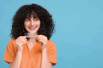 Young woman holding teeth whitening strips on light blue background, space for text