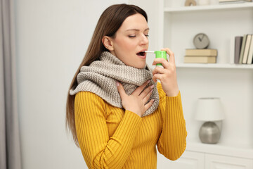 Adult woman with scarf using throat spray at home - obrazy, fototapety, plakaty