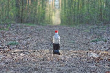 one plastic bottle with a black drink lemonade stands on gray ground on a road in the spring forest