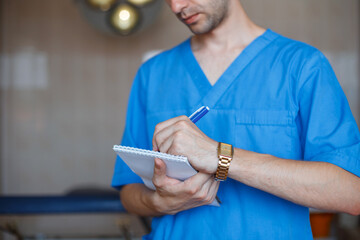 A doctor in a blue uniform writes down a diagnosis and recommendations in a notebook.