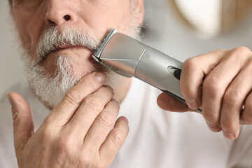 Man trimming mustache with electric trimmer indoors, closeup - obrazy, fototapety, plakaty