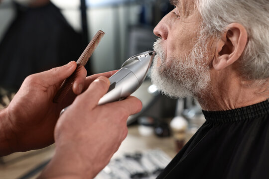 Professional barber trimming client's mustache in barbershop, closeup