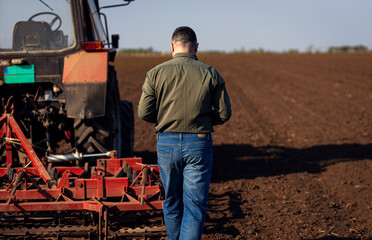 Rear view of mature farmer standing in field preparing to cultivate the land with a tractor.