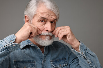 Senior man touching mustache on grey background