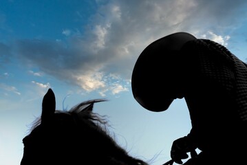 Silhouette of a woman in a cowgirl hat on a horse on clouds background