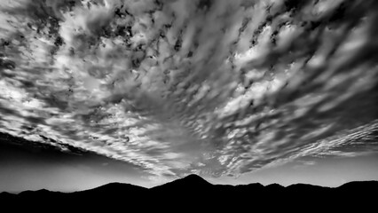 Black and white shot of a cloudy sky with silhouettes of mountains below