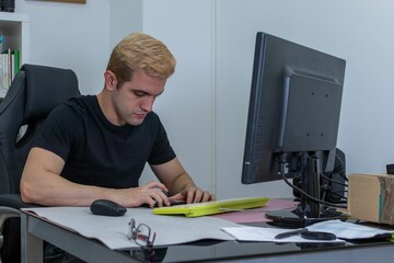 Blonde young man concentrated while working on his computer in the office - a corporate concept