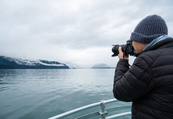 Tourist taking photos using a DSLR camera. Boat cruising Resurrection Bay, Kenai Fjords, Seward, Alaska. - 782948983