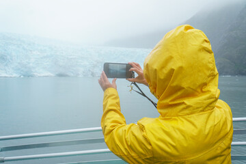 Tourist taking smartphone photos of Holgate Glacier in the rain. Kenai Fjords National Park,...