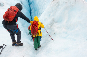 Tourists helping each other and climbing down the glacier crevasse using ropes. Exit Glacier ice...