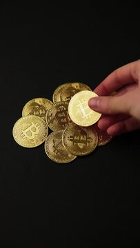 Hand leaving a bitcoin on a pile of bitcoins golden coins on a black background, vertical shot. Bullish BTC, cryptocurrency, 2p2 exchange and blockchain concept