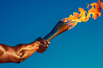 A close-up of an athlete's hand holding the olympic torch stands solemnly against the blue sky.  space for copying.