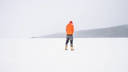 Man with an orange winter Jacket standing on a snow-covered hill