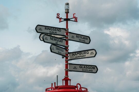 Red sign pole with compass directions showing ways to multiple big cities around the world