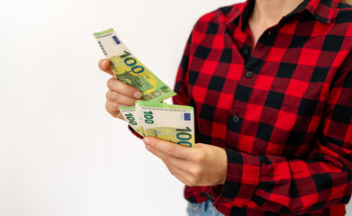 Female person in casual red shirt counts money in her hands. 100 euro bills in woman's hands.