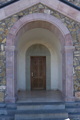 Carved wooden door of the Saint Peter and Paul monastery. Carved stone arch with patterns and bas-relief of saints. Brown stone arch and steps. View from outside of the church. Georgia
