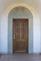 Carved wooden door of the Saint Peter and Paul monastery. Carved stone arch with patterns and bas-relief of saints. View from inside of the church. Georgia