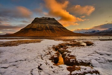 Scenic shot of a rocky hill at sunset with snow on its foot