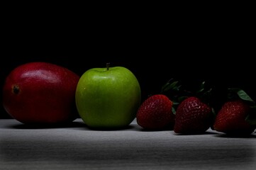 Closeup of two apples and three strawberries on the dark background